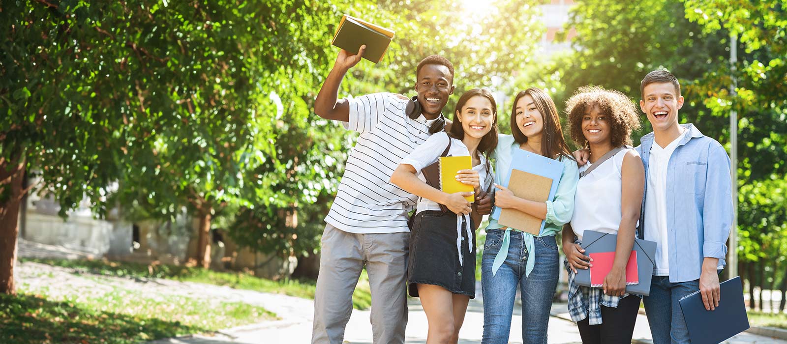 Group of multicultural university students posing outdoors after study, sincerely smiling